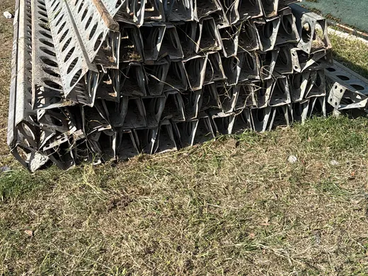 Vigas E-Beam perforadas acopiadas sobre el pasto, listas para cargar